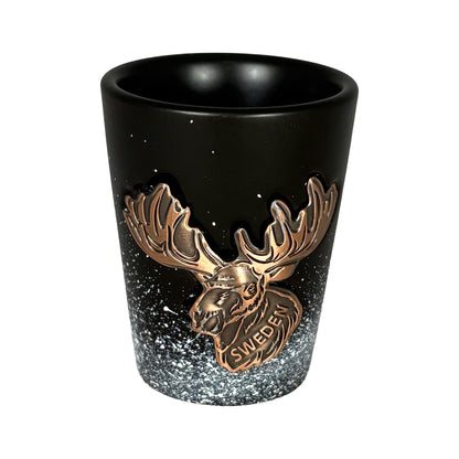 Svart shotglas med bronsfärgat älghuvud och texten "Sweden", designat med snöflingemotiv som skapar en känsla av svensk vintermagi. En elegant och rustik souvenir som symboliserar svensk natur och kultur.