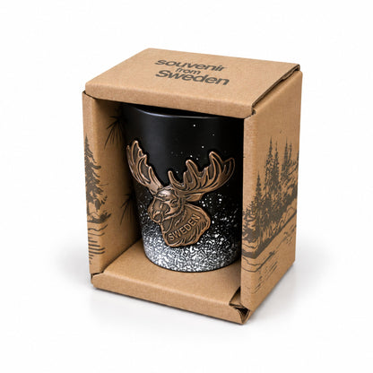 Svart shotglas i brun pappförpackning med mörkbrunt skogsmotiv och texten "Souvenir from Sweden" på toppen.