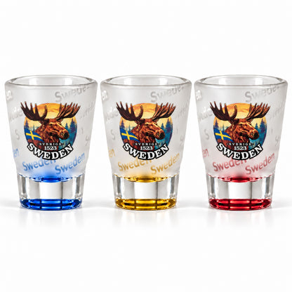  Tre frostade shotglas med älghuvud och texten "Sweden" – ett med röd botten, ett med gul och ett med blå.
