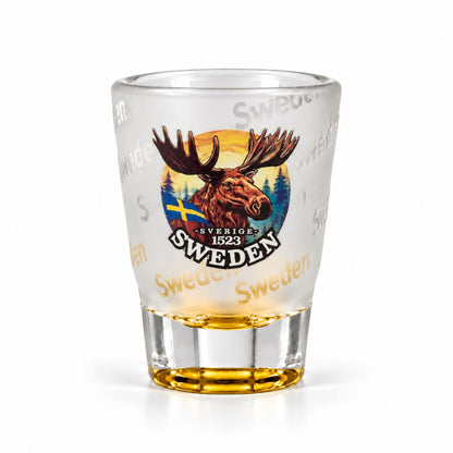 Frostat shotglas med gul botten, motiv av ett ståtligt älghuvud och texten "Sweden" flera gånger runt glaset.