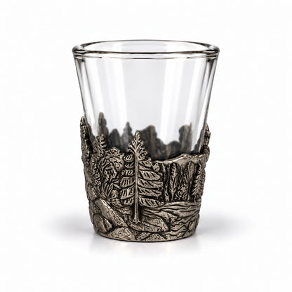 Shotsglas i glas med ett omslag i tennfärgad metall med skogsmotiv. 