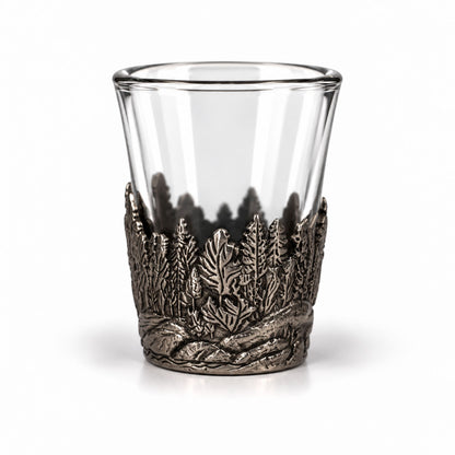 Shotsglas i glas med ett omslag i tennfärgad metall med skogsmotiv. 