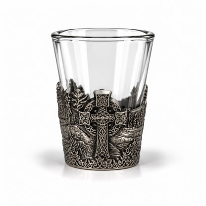 Shotsglas i glas med ett omslag i tennfärgad metall med vikingamotiv. Här syns ett keltiskt kors.