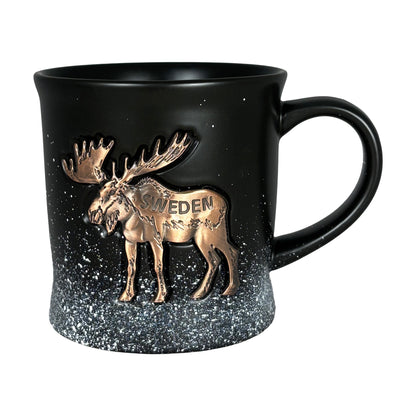 Svart mugg med bronsfärgad älg och texten "Sweden", designad med snöflingemotiv som skapar en känsla av svensk vintermagi. En elegant och rustik souvenir som symboliserar svensk natur och kultur.