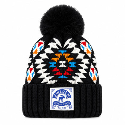 Svart stickad mössa med tofs och mönster i vitt, blått, rött och orange, dekorerad med texten. Framme på mössan finns ett märke med motiv av en älg och texten "Sweden Northern Country"