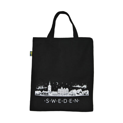 Svart tygkasse med vit skyline som visar typiska svenska motiv, bland annat älg, midsommarstång, sjöbodar, Stockholms stadshus och vikingaskepp. Texten "Sweden" och "Sverige" pryder kassen, och kanten är dekorerad med den svenska flaggan.